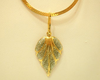 May include: A gold chain necklace with a gold leaf pendant. The leaf is textured with a sparkly finish.