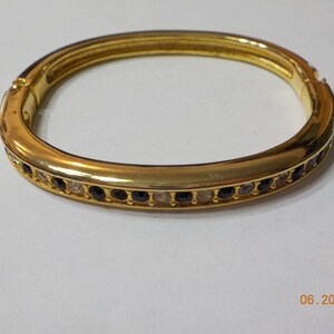May include: A gold bangle bracelet with a row of black and clear rhinestones.