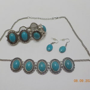 May include: A turquoise and silver jewellery set with a necklace, bracelet, and earrings. The necklace and bracelet feature oval turquoise stones with silver accents. The earrings are small and feature oval turquoise stones.