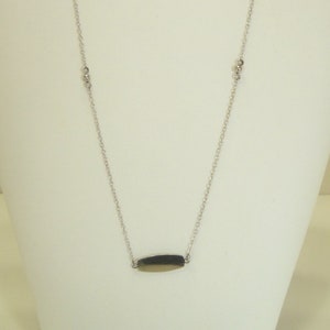May include: A silver chain necklace with a small, oval-shaped pendant. The chain has small, round accents.