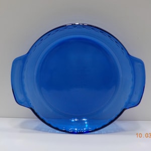 May include: A round, cobalt blue glass serving dish with two handles. The dish has a smooth, glossy surface and a decorative rim. The date "10.03.2025" is visible in the bottom right corner. This dish is suitable for serving food.