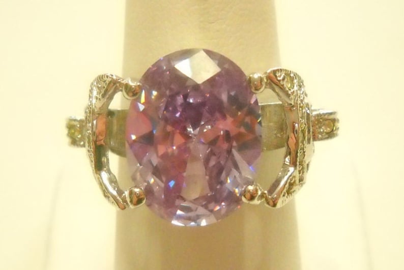 May include: A silver ring with a large oval-shaped purple gemstone surrounded by smaller clear gemstones.