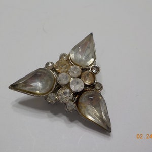 May include: A silver tone brooch with a triangular shape and a cluster of clear and iridescent rhinestones.