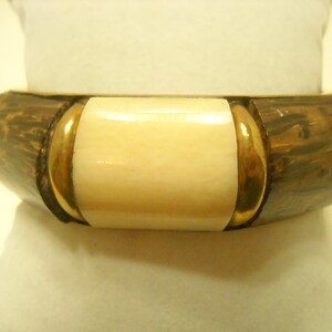 May include: A brown and gold bangle bracelet with a white rectangular inlay. The bracelet is made of wood and metal.