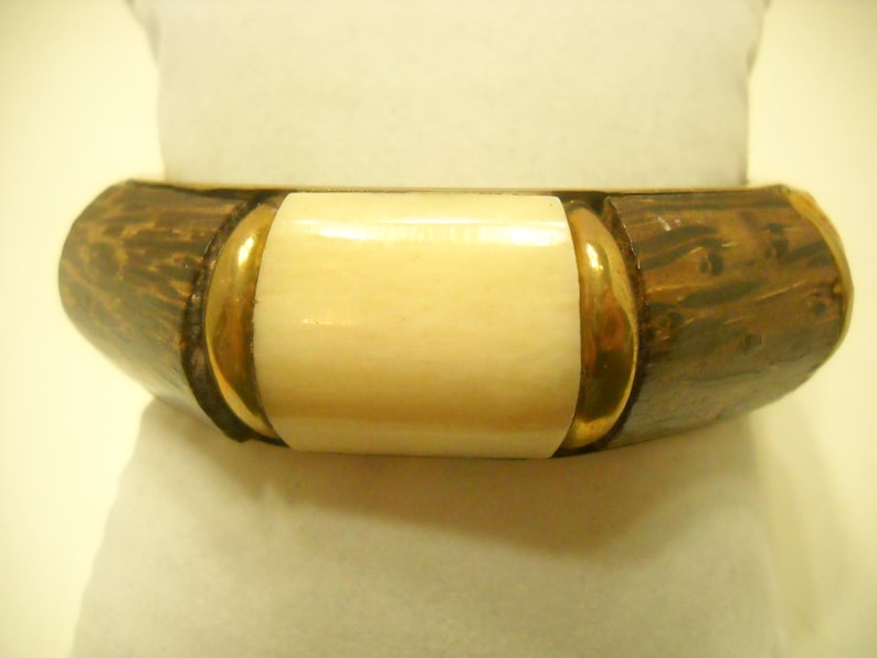 May include: A brown and gold bangle bracelet with a white rectangular inlay. The bracelet is made of wood and metal.