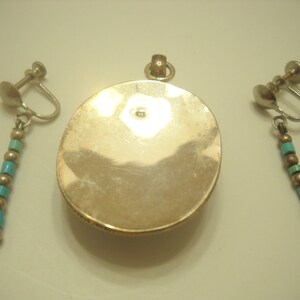 Op de afbeelding: Een zilveren hanger met een turquoise steen en bijpassende clip-on oorbellen met turquoise kralen.