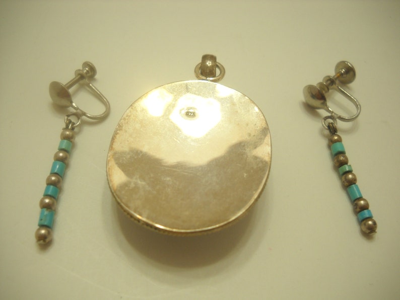 Op de afbeelding: Een zilveren hanger met een turquoise steen en bijpassende clip-on oorbellen met turquoise kralen.