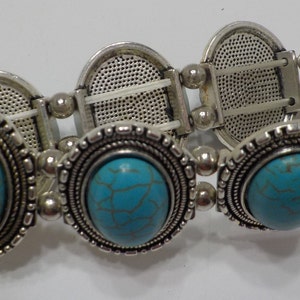 May include: A silver bracelet with turquoise stones. The bracelet has a stretchy band and is decorated with ornate silver accents.
