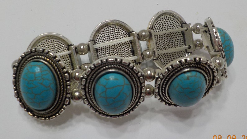 May include: A silver bracelet with turquoise stones. The bracelet has a stretchy band and is decorated with ornate silver accents.