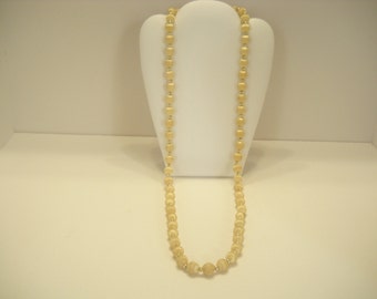 May include: A long, cream-colored beaded necklace with a satin finish. The necklace is displayed on a white mannequin bust.