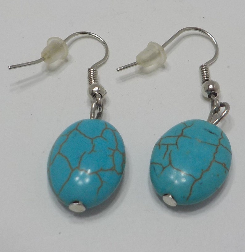 May include: A pair of silver dangle earrings with turquoise oval-shaped stones. The stones have a marbled pattern.