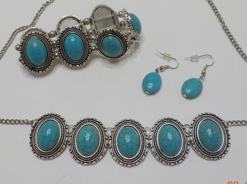 May include: A turquoise and silver jewellery set with a necklace, bracelet, and earrings. The necklace and bracelet feature oval turquoise stones set in silver frames. The earrings are silver with turquoise stones.