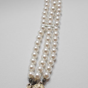 May include: A triple strand pearl bracelet with a decorative clasp featuring a pearl surrounded by rhinestones.