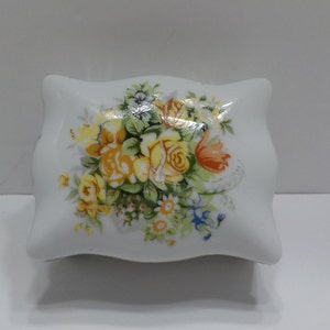 May include: White porcelain trinket box with a floral design featuring yellow, orange, and green flowers.