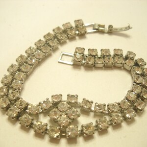 May include: A silver tone rhinestone bracelet with a double row of clear stones and a clasp closure.