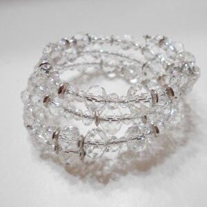 May include: A clear crystal coil bracelet with multiple strands. The bracelet features faceted crystal beads and silver-toned metal accents. The design wraps around the wrist, creating a sparkling, elegant accessory.
