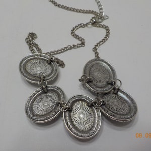 May include: A silver necklace with four oval-shaped pendants. The pendants have a textured, circular design.