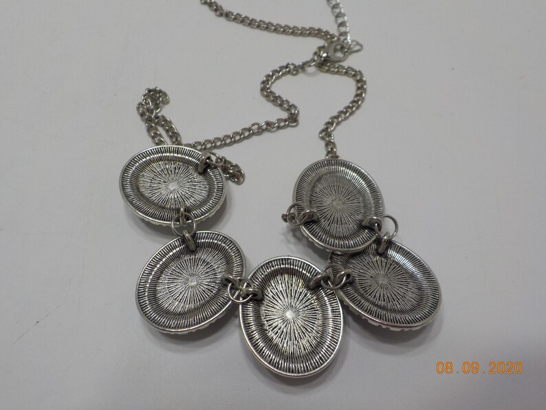 May include: A silver necklace with four oval-shaped pendants. The pendants have a textured, circular design.