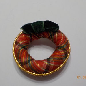 May include: A small red, green, and gold plaid fabric wreath with a green velvet bow.