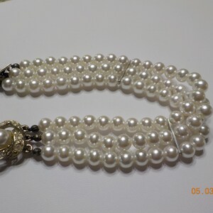 May include: A triple strand pearl necklace with a silver clasp and a decorative silver and rhinestone pendant.