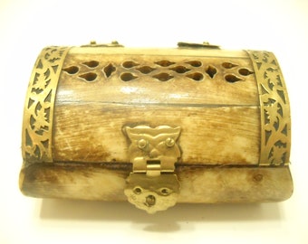May include: A small, rectangular box made of bone with intricate brass detailing. The box has a hinged lid with a brass clasp in the shape of a stylized owl. The box is decorated with a repeating pattern of brass leaves and flowers.