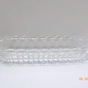 May include: Clear glass oval serving dish with a scalloped rim and textured base. The dish is designed for serving food and is suitable for various occasions. The clear glass allows the contents to be visible.