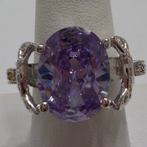 May include: A silver ring with a large, oval-shaped, purple gemstone. The ring has intricate details on the band.