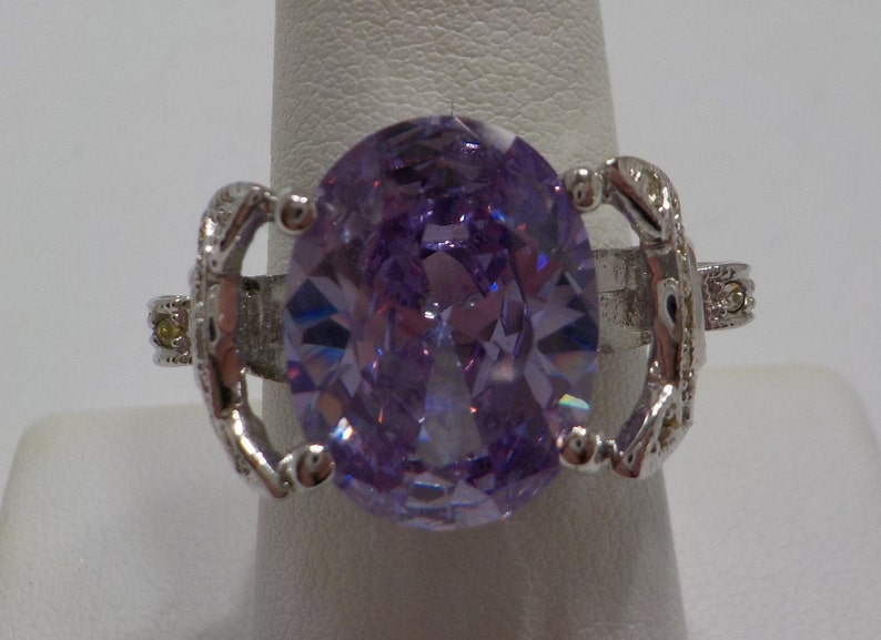 May include: A silver ring with a large, oval-shaped, purple gemstone. The ring has intricate details on the band.