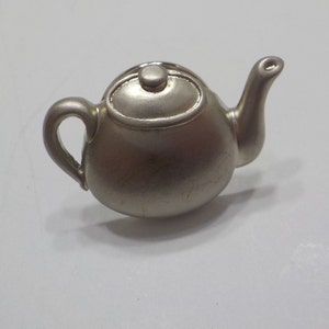 May include: A silver teapot with a rounded body and a small spout. The teapot has a lid with a small knob on top.
