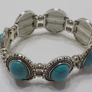 May include: A silver stretch bracelet with turquoise stones. The bracelet has a decorative design on the metal.