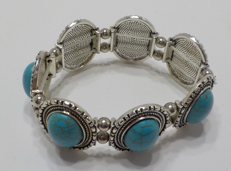 May include: A silver stretch bracelet with turquoise stones. The bracelet has a decorative design on the metal.