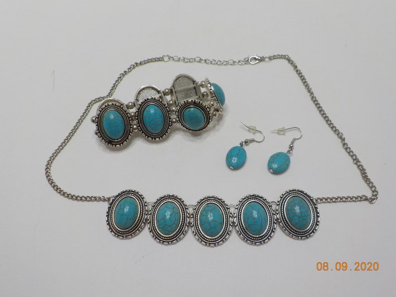 May include: A turquoise and silver jewellery set with a necklace, bracelet, and earrings. The necklace and bracelet feature oval turquoise stones with silver accents. The earrings are small and feature oval turquoise stones.