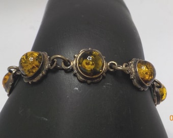 May include: A silver-toned link bracelet featuring five round, translucent amber-colored cabochons set in scalloped metal bezels. The stones display internal golden-brown inclusions and are connected by small circular metal jump rings.
