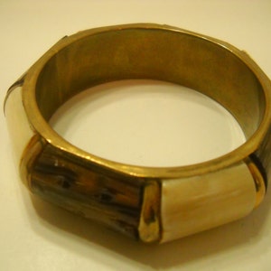 May include: A gold bangle bracelet with brown and white geometric patterns.