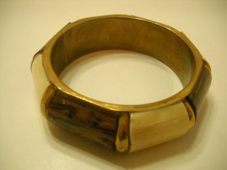 May include: A gold bangle bracelet with brown and white geometric patterns.