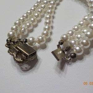 May include: A three-strand pearl necklace with a silver clasp. The clasp is ornate and features a floral design.