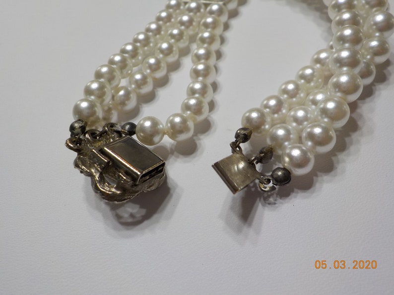 May include: A three-strand pearl necklace with a silver clasp. The clasp is ornate and features a floral design.