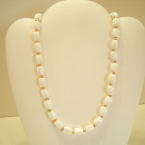 May include: A white and gold beaded necklace with square-shaped beads. The necklace is displayed on a white mannequin bust.