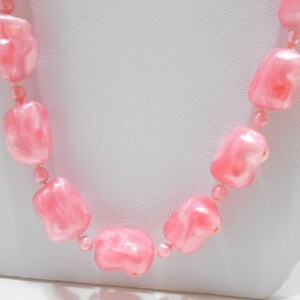 May include: A pink beaded necklace with large, irregular shaped beads. The beads have a marbled, translucent appearance.