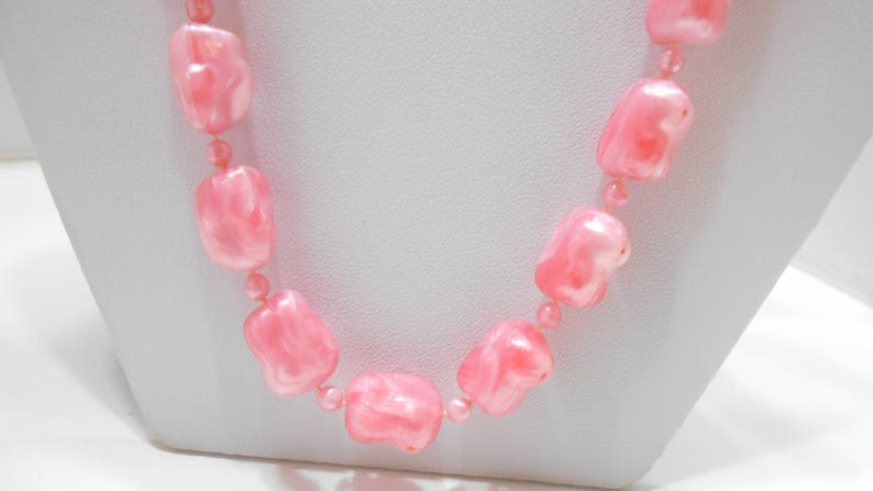 May include: A pink beaded necklace with large, irregular shaped beads. The beads have a marbled, translucent appearance.