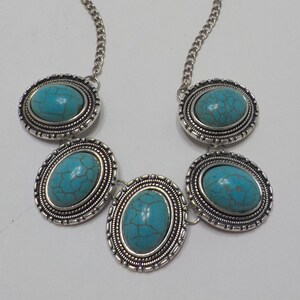 May include: A silver necklace with five turquoise oval stones set in ornate silver frames. The necklace has a silver chain.