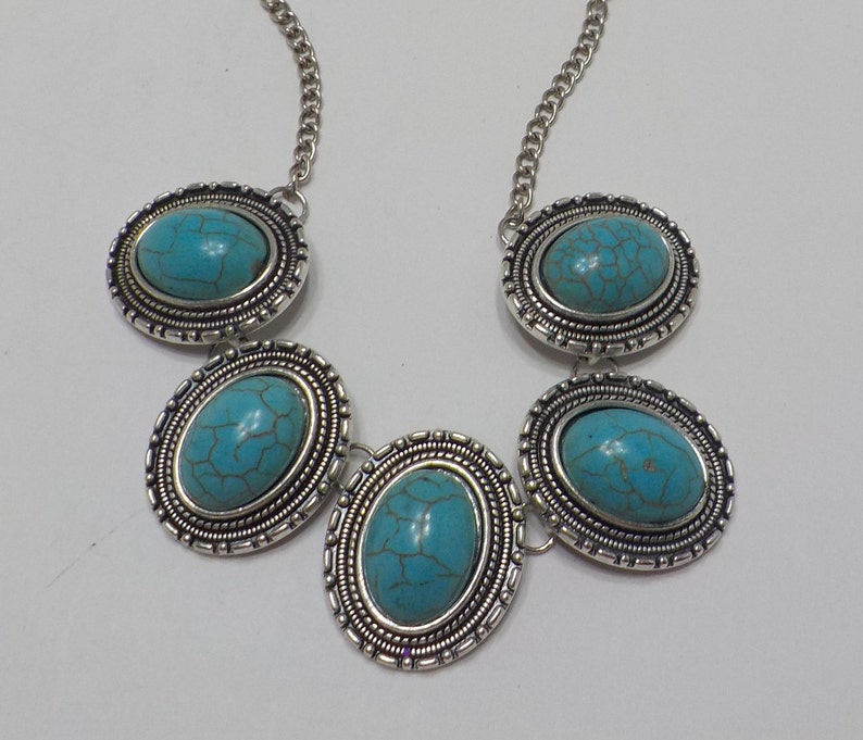 May include: A silver necklace with five turquoise oval stones set in ornate silver frames. The necklace has a silver chain.