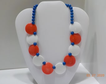 May include: A necklace with large, round, red, white, and blue beads. The beads are strung on a blue cord.