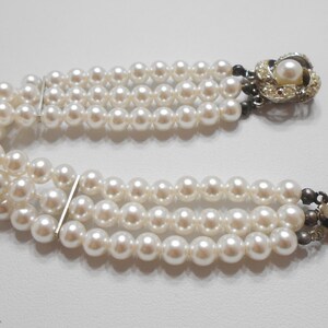 May include: A triple strand pearl bracelet with a decorative clasp featuring a faux pearl and rhinestones.