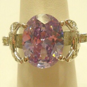 May include: A silver ring with a large, oval-shaped, light purple gemstone set in a decorative, ornate setting.