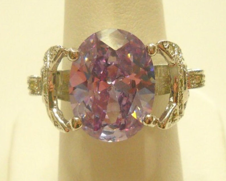 May include: A silver ring with a large, oval-shaped, light purple gemstone set in a decorative, ornate setting.