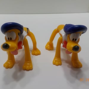 Puede incluir: Dos perros de juguete de plástico amarillo que llevan sombreros azules y camisas blancas con pajaritas rojas. Los perros están en una pose juguetona con la lengua fuera.