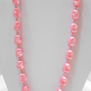 May include: A pink pearl necklace with square-shaped beads. The necklace is displayed on a white mannequin bust.