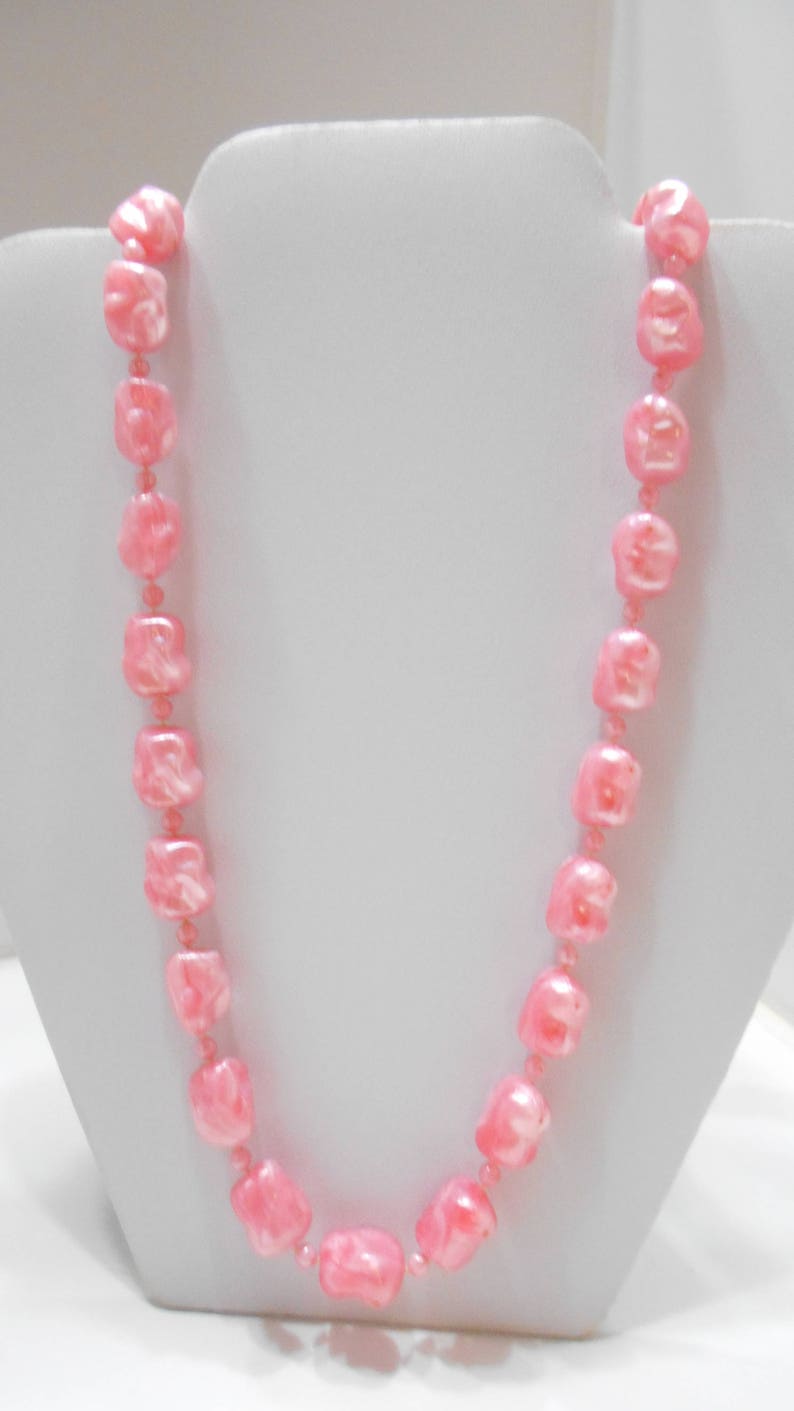 May include: A pink pearl necklace with square-shaped beads. The necklace is displayed on a white mannequin bust.