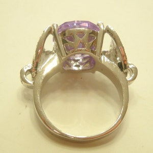 May include: A silver ring with a large, clear, purple gemstone set in a decorative, open-work setting.